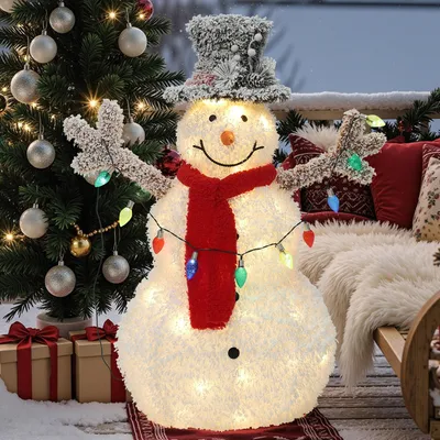 A lighted snowman decoration with a Christmas tree and gifts in a snowy outdoor setting.