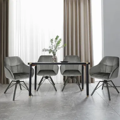 Four gray velvet dining chairs arranged around a dark wooden dining table with a vase of greenery and a plate on top.