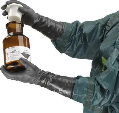 A person wearing protective gear and gloves is holding a chemical bottle.