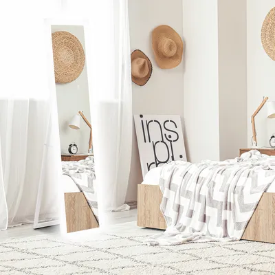 A bedroom scene with a full-length mirror, bed, and decorative hats.