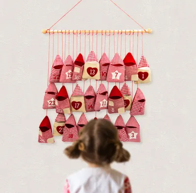 A child looks at a hanging advent calendar with small red and white fabric bags.