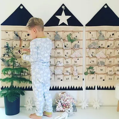 A young boy in pajamas is looking at a fabric advent calendar with 24 pockets filled with small gifts.
