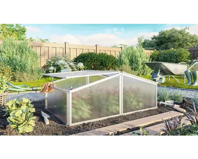 A small greenhouse in a garden setting, surrounded by plants, a fence, and gardening tools.