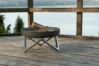A fire pit with logs on a wooden deck overlooking a body of water and trees.