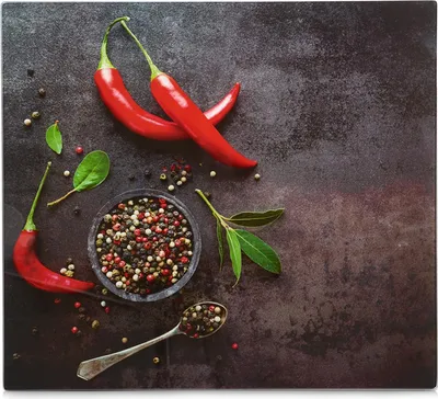 A top-down view of red chili peppers, peppercorns in a bowl and on a spoon, and bay leaves on a dark, textured surface.
