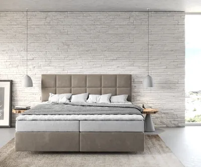 A modern bedroom with a box spring bed against a white brick wall.