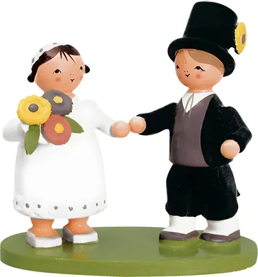 Miniatur aus Holz zeigt ein Brautpaar mit schwarzem Anzug weissem Kleid Braut mit Schleier und Blumenstrauß Bräutigam mit Zylinder nebeneinander stehend auf einem grünen Holzsockel
