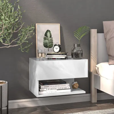 A white floating nightstand with books and decor next to a bed.
