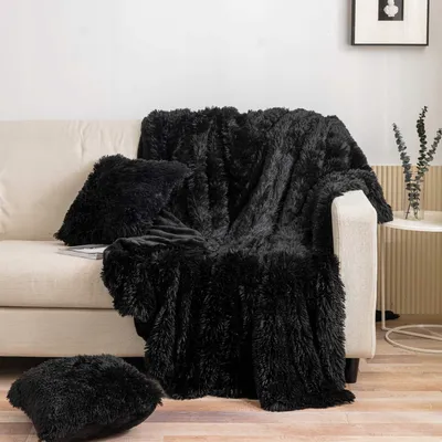 A black furry blanket and two pillows are draped over a cream-colored sofa in a living room setting.