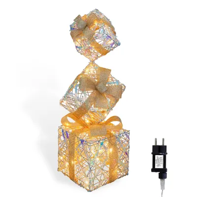 A stack of three illuminated gift boxes with gold bows, shown against a white background. A power adapter is visible to the right.