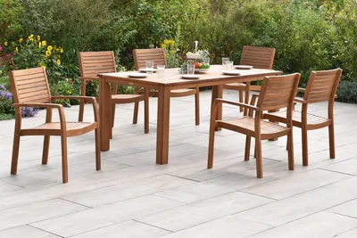 An outdoor dining set with a wooden table and chairs on a patio, surrounded by greenery and flowers.
