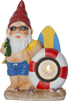 A garden gnome dressed for the beach, holding a bottle and standing next to a surfboard and a life preserver with a solar light.