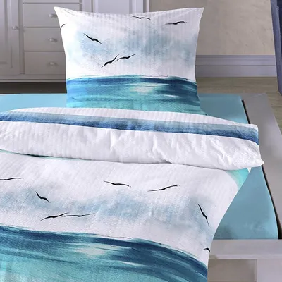 A close-up view of bedding with a coastal theme, featuring a watercolor-style print of the ocean and seagulls.