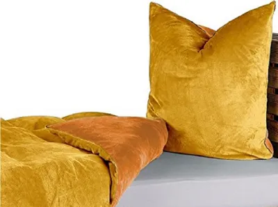 A close-up view of a gold pillow and a folded blanket with an orange underside, placed on a surface.