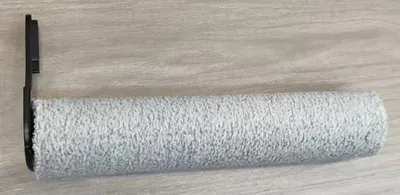 A cleaning roller brush with a black plastic attachment on a wooden surface.