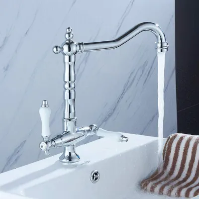 A chrome kitchen faucet with white ceramic handles is shown in a bathroom or kitchen sink, with water running.