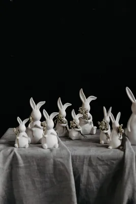 A collection of white ceramic Easter bunny figurines arranged on a grey tablecloth against a black background.