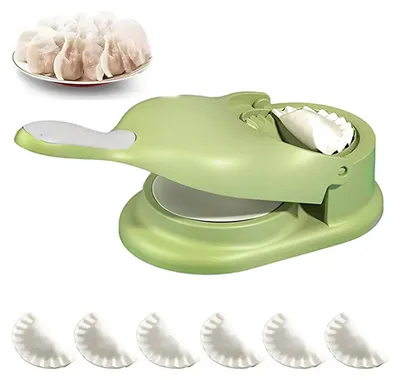 A green dumpling maker with a plate of dumplings in the background and several finished dumplings in the foreground.