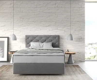 A bedroom scene with a bed against a textured white brick wall.