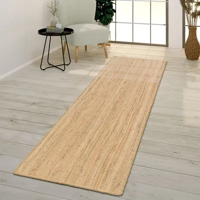 A runner rug is placed on a light wooden floor in a room with a chair and a side table.