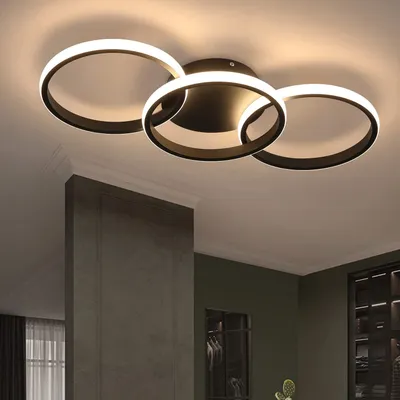 A modern ceiling light fixture with three interlocking rings, illuminated by warm white LEDs, installed in a room with a dark green wall and a concrete pillar.
