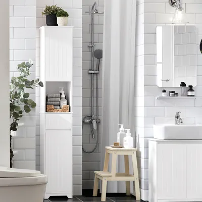 A clean, modern bathroom with white tiled walls, featuring a tall white storage cabinet, a shower, and a sink.