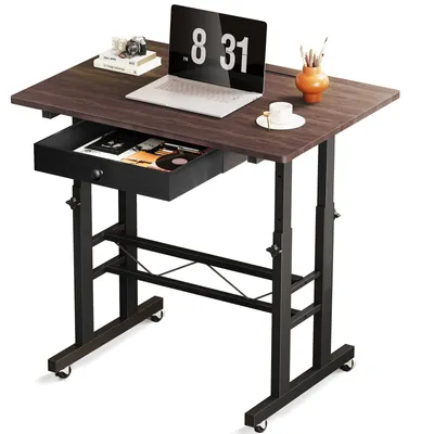 A close-up, slightly angled shot of a brown and black adjustable desk with a laptop, books, and art supplies on it.