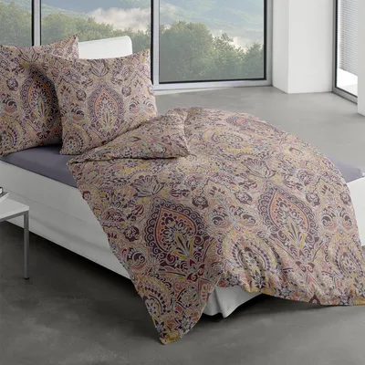 A bed with patterned bedding and pillows in a room with a large window overlooking a landscape.