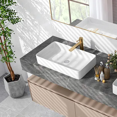 A modern bathroom vanity with a white ceramic vessel sink, gold faucet, and decorative items.