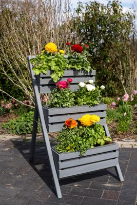 A tiered planter filled with colorful flowers on a paved patio.