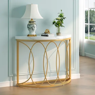 A console table with a marble top and gold metal frame, decorated with a lamp and flowers, placed against a light blue wall next to a window.