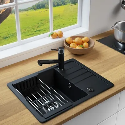 A kitchen sink with a faucet, a drying rack, and a bowl of oranges on a wooden countertop, with a window overlooking a green landscape in the background.