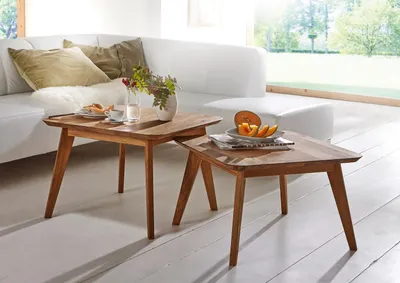 A living room scene with a white sofa and two wooden side tables, one with a vase of flowers and a cup of coffee, the other with fruit.