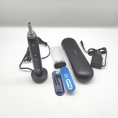 A black Oral-B iO electric toothbrush and its accessories are laid out on a white surface.