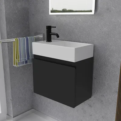 A modern bathroom vanity with a black cabinet and white sink, mounted on a gray tiled wall. Towels hang on a rack to the left.