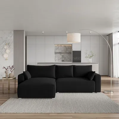 A modern living room scene with a black sectional sofa and a kitchen area in the background.