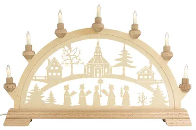 Ein traditioneller Schwibbogen aus Holz zeigt eine winterliche Szene mit einer Kirche Bäumen und Figuren die Kerzen tragen während elektrische Kerzen auf dem Bogen leuchten