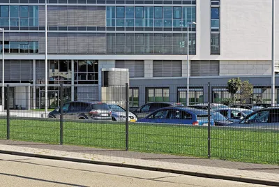 A fence in front of a modern office building with cars parked in the background.