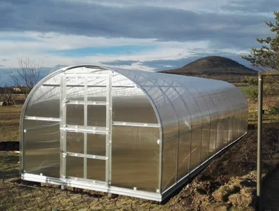 A greenhouse is set up in an outdoor area with a hill and cloudy sky in the background.