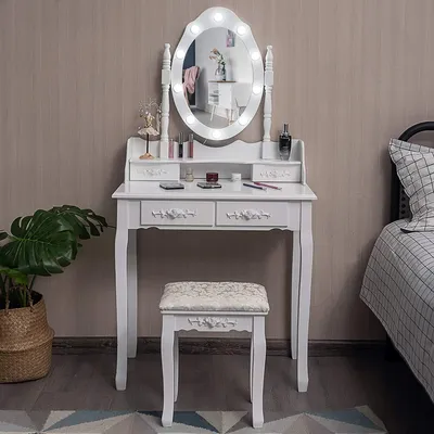 A white vanity table with a lighted mirror and a stool, set up in a room.