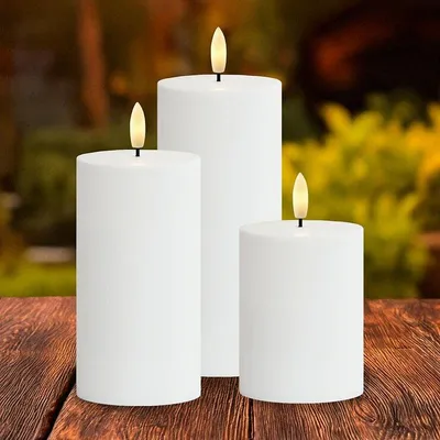 Three white LED candles with flickering flames are arranged on a wooden table outdoors.