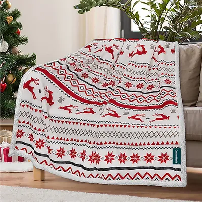 A Christmas-themed blanket with reindeer and snowflake patterns is draped over a couch next to a decorated Christmas tree.