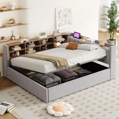 A modern bedroom with a grey upholstered bed featuring a built-in headboard with shelves. The bed has storage drawers underneath, and is made up with white bedding and a beige throw blanket.
