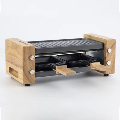 A raclette grill with wooden accents and two black pans is shown against a white background.