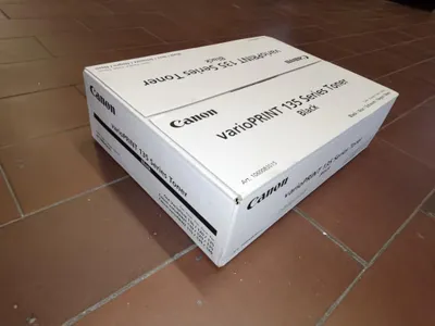A white Canon toner cartridge box is placed on a tiled floor.