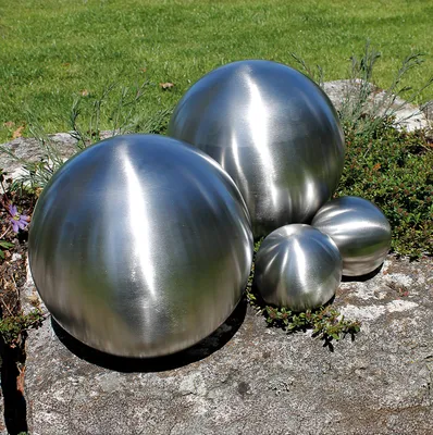 Four metallic spheres of varying sizes are placed on a stone surface with grass and low-lying plants in the background.