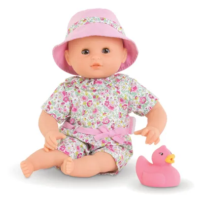 A baby doll wearing a floral outfit and a pink hat, sitting next to a pink rubber duck.