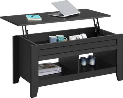 A black lift-top coffee table with a laptop and notebook on the raised surface, and mugs and headphones inside the storage compartment. The lower shelf holds books and decorative candles.