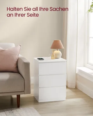 A white nightstand with three drawers is placed next to a sofa in a room. A lamp and a phone are on top of the nightstand.