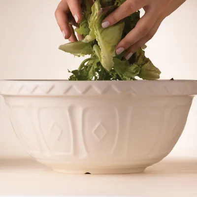 Hands adding lettuce to a white mixing bowl.